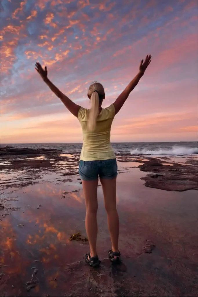 Jeune femme admirant un coucher de soleil rosé au bord de l'eau