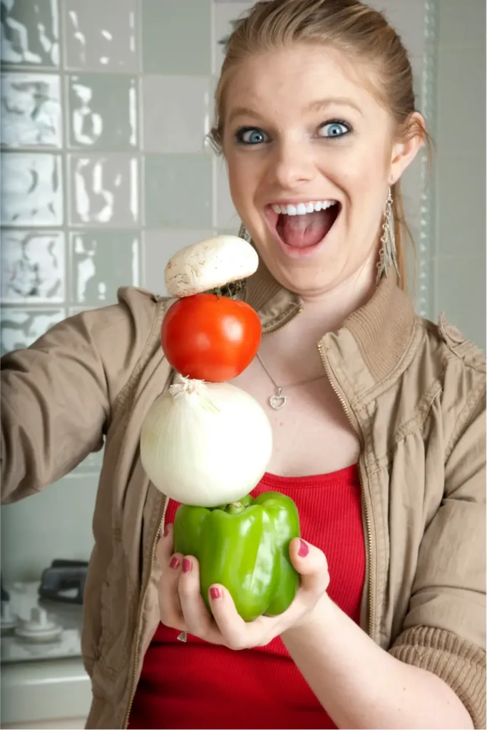 Jeune femme souriante et pleine d'énergie dans sa cuisine avec une pile de légumes frais